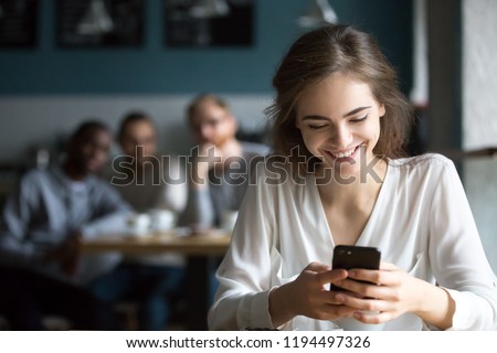 Pretty young girl sit in café using smartphone laughing because of flirting students from behind table, happy female smiling feeling attention from males talking to her. Love from first sight concept Royalty-Free Stock Photo #1194497326