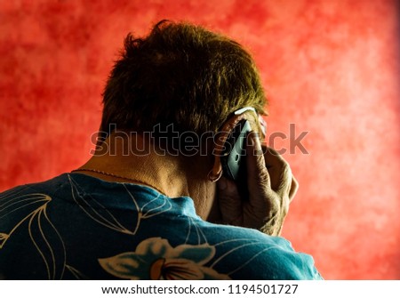 Hands of an elderly man with a phone. An elderly woman talking on a cell phone. Back view. Red background. Royalty-Free Stock Photo #1194501727