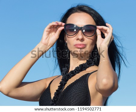 Female person at the sea. Dark haired woman in one-piece swimsuit adjusting sunglasses and looking at camera