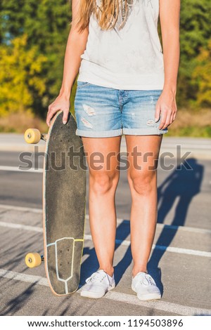 Beautiful young woman wearing jeans shorts, posing with skateboard in hand