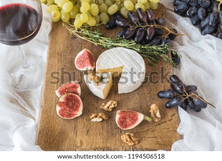 Top view on a wooden tray there is an assortment of camembert cheese along with sliced ​​figs and grapes