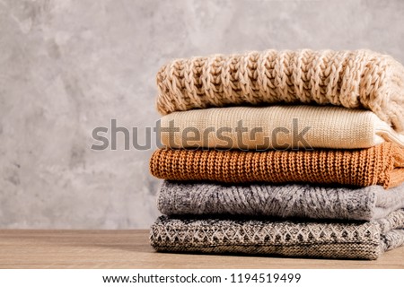 Bunch of knitted warm pastel color sweaters with different knitting patterns folded in stack on brown wooden table, grunged texture wall background. Fall winter season knitwear. Close up, copy space Royalty-Free Stock Photo #1194519499