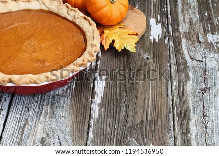 Homemade pumpkin pie in red ceramic pie plate over a rustic wooden background. Extreme shallow depth of field with selective focus.