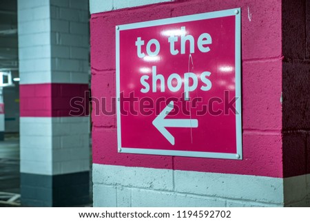 to the shops pink directional sign on brick column in shopping centre car park