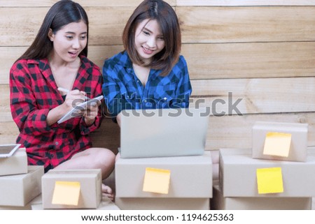 Two young woman start up their SME business. Businesswoman teamwork private working at home office using laptop write order on book. Packaging delivery online shopping service advertising to customer.