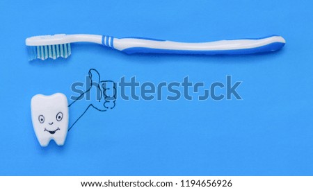 A fun tooth figurine puts a toothbrush class on a blue background. The view from the top. Flat lay.