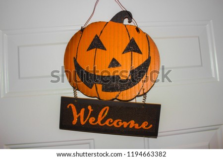 A halloween welcome pumpkin sign hanging on a white door.