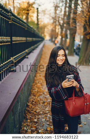 girl using her cell phone while walking through the park during autumn