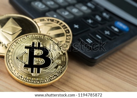 Golden physical Bitcoin, Ethereum and Litecoins on calculator on wooden background. Cryptocurrency market numbers abstract concept.
