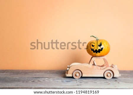 Wooden toy car with funny evil pumpkin on the roof on orange background. Space for text. Halloween background.

