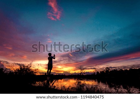 silhouette of man taking pictures with his smartphone at sunset.