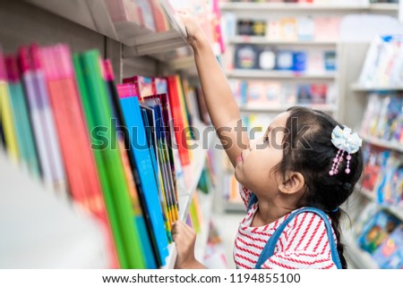 Cute asian child girl select book on bookshelf in bookstore in supermarket