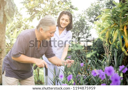 Comforting hand. Young nurse holding old man's shoulder in outdoor garden looking at flower. Senior care, care taker and senior retirement home service concept. Royalty-Free Stock Photo #1194875959