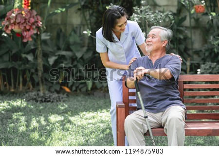 Nurse with patient sitting on bench together talking. Asian old man sitting on bench and young woman carer talking to him. Happy smile. Royalty-Free Stock Photo #1194875983