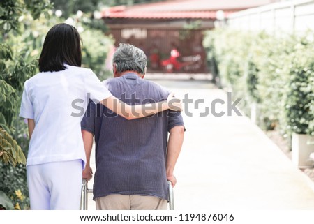Nurse with patient using walker in retirement home. Young female nurse holding old man's shoulder in outdoor garden walking. Senior care, care taker and senior retirement home service concept. Royalty-Free Stock Photo #1194876046