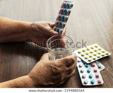 An elderly woman drinks medicines and vitamins. Hands of an elderly person with a mug of water. Healthcare concept. Royalty-Free Stock Photo #1194880564
