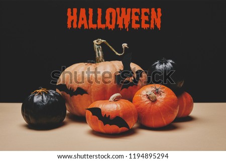 orange and black pumpkins with paper bats on table with "halloween" sign