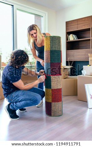 Couple unpacking moving boxes and unrolling the carpet