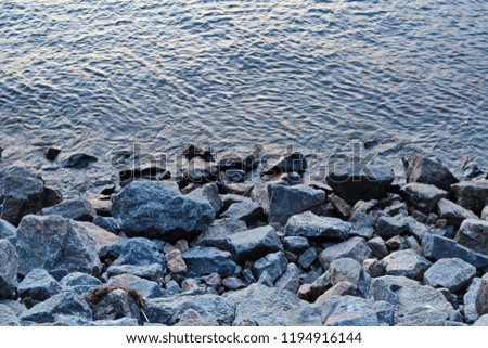 Sea shore with big sharp pebble and water in half on sunset