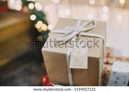 Close up of a Kraft Christmas gift and a greeting card on a ribbon in a Santa Claus sleigh against a background of lights.