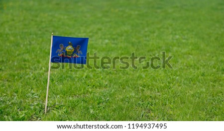 Pennsylvania flag. Photo of Pennsylvania state flag on a green grass lawn background. Close up of US state flag waving outdoors.
