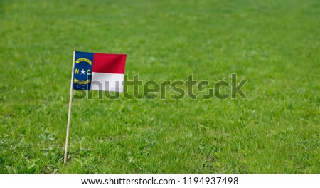 North Carolina flag. Photo of North Carolina state flag on a green grass lawn background. Close up of state flag waving outdoors.