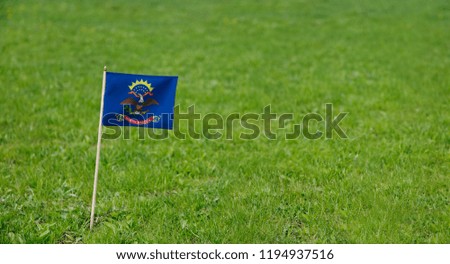 North Dakota flag. Photo of state flag on a green grass lawn background. Close up of state flag waving outdoors.