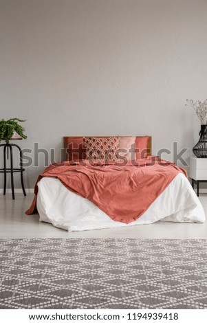 Patterned carpet in grey bedroom interior with red sheets on bed between plants. Real photo