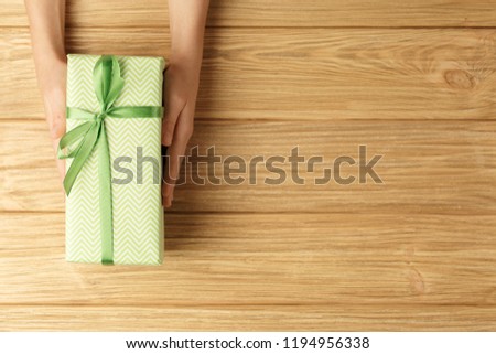 gift box in the hands on a wooden background top view, flat lay festive concept, female hands with green box with a gift