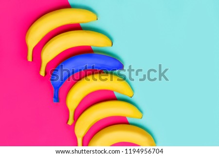 Bright blue banana among yellow fruits on pink and pastel blue background, top view