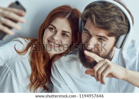 man in headphones next to a woman look into the phone                          