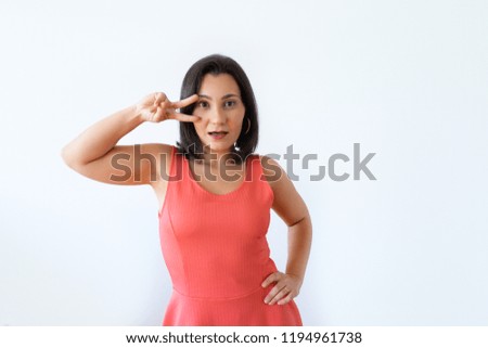 Surprised Indian woman dancing with open mouth. Portrait of shocked girl showing peace sign near eye and looking at camera. Isolated on white. Dancing concept