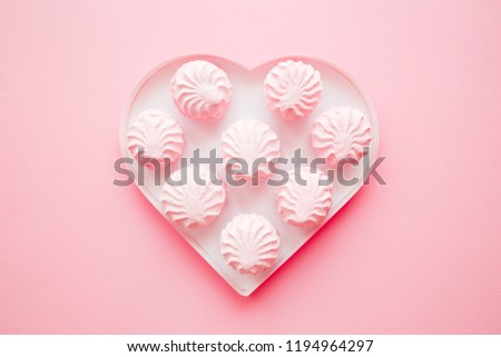 Fluffy, airy zephyrs in box of heart shape for beloved on pastel pink table. Love sweets. Mockup for different ideas. Top view.