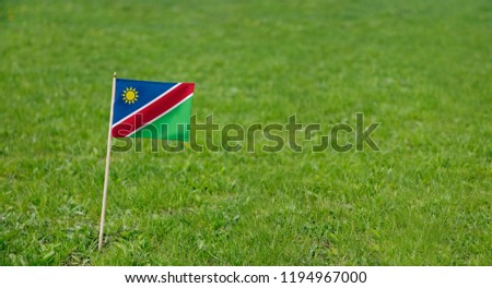 Namibia Flag. Photo of Namibia flag on a green grass lawn background. National flag waving outdoors.