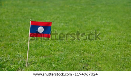 Laos Flag. Photo of Laos flag on a green grass lawn background. National flag waving outdoors.