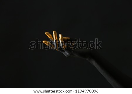 Hand of woman with black and golden paint on her skin against dark background