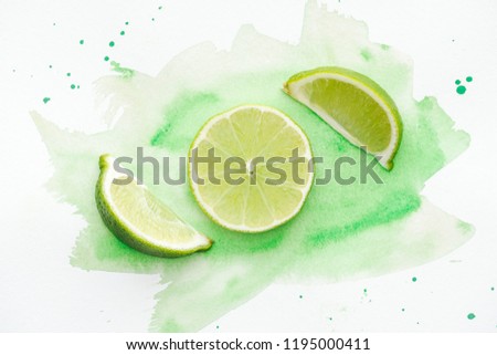 top view of pieces of green ripe limes on white surface with green watercolor