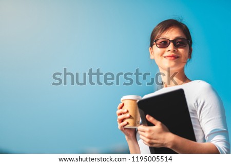 Business woman with coffee and tablet on hand walking on waterfront with Hong Kong cityscape in background.