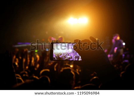 Man taking smart phone at live concert and lights on stage.