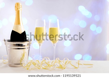 Champagne bottle in champagne cooler with filled glasses for a party in front of a colorful blurred background