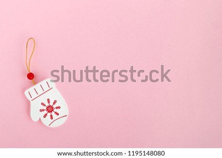 Wooden Christmas and New Year decoration in the form of mitten with painted red snowflake on a pink background, top view.