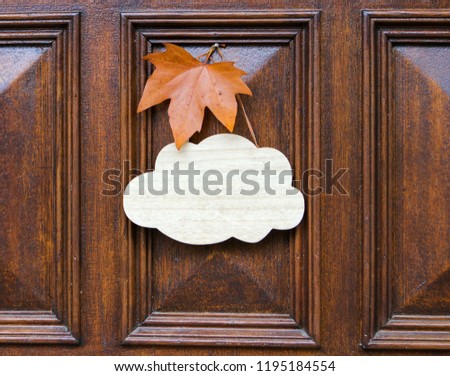Mock up, welcome empty table sign of cloud shape decorated with orange maple leaf hanging on dark wooden entrance door. Welcome autumn. Copy space