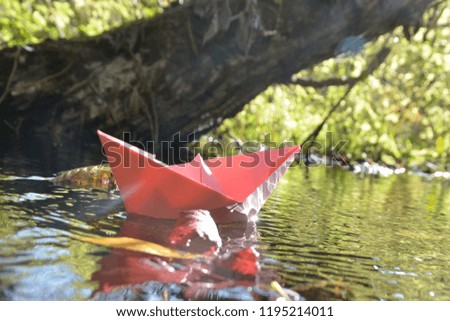 Pink paper ship floats in stagnant water between plants in autumn in Germany