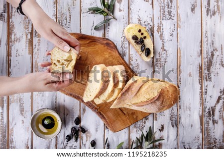Female hands serving traditional Greek Appetizer olives with bread, olive oil  and balsamic vinegar, over rustic olive wooden board over a white wooden background. Top View