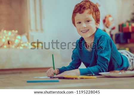 My hobby. Positive delighted kid lying on the floor while drawing picture