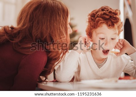 Fantastic picture. Close up of surprised little child holding a pencil and looking at his drawing while his mother sitting near him
