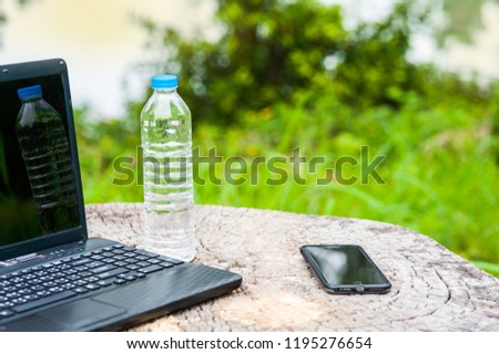 Computer and smartphone and water bottle on wooden timber