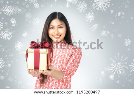 Photo of asian curious woman in red dress enjoy new year gift box. Young woman holding gift  box with red bow being excited and surprised  holiday present isolated white background and snowflake.