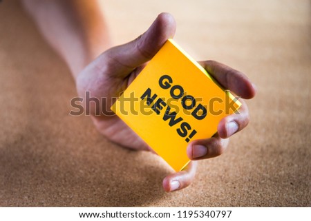 a hand holding a colored paper note with the phrase GOOD NEWS