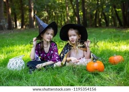 two girls in carnival costumes of fairies, witches are sitting on the grass and celebrate the holiday Halloween